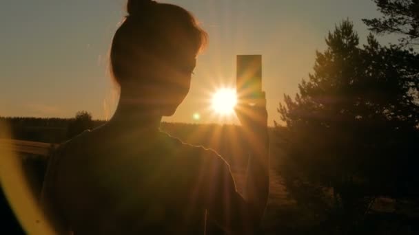 Женский силуэт фотографирует закат со смартфоном — стоковое видео