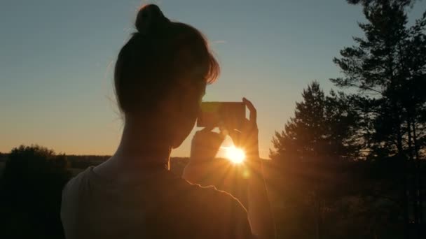 Mujer silueta tomando fotos de increíble puesta de sol con teléfono inteligente en el parque — Vídeo de stock