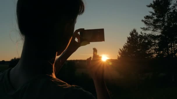 Kadın silueti akıllı telefonla gün batımının fotoğrafını çekiyor. — Stok video