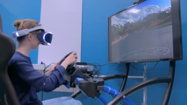 Sanal gerçeklik kulaklığı kullanan ve araba sürücüsü simülatöründe oynayan genç bir kadın.