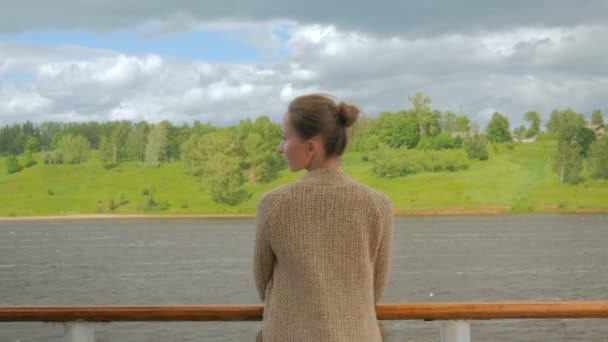 Молодая женщина стоит на палубе круизного судна и смотрит на реку и пейзаж — стоковое видео