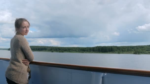 Молодая женщина стоит на палубе круизного судна и смотрит на реку и пейзаж — стоковое видео