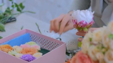Çiçekçide çiçeklerle hediye kutusu yapan profesyonel bir çiçekçi.