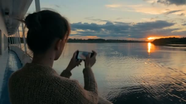 Женский силуэт фотографирует закат со смартфоном на палубе круизного лайнера — стоковое видео