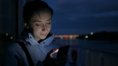 Geceleri cruise gemi güvertesinde dikey smartphone kullanan kadın