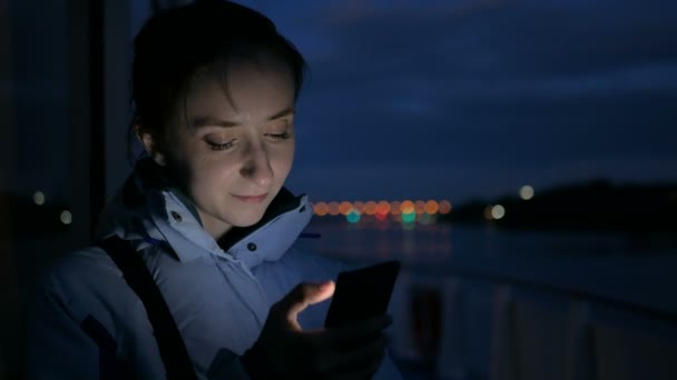 Vrouw met behulp van verticale smartphone op het dek van een cruiseschip nachts — Stockvideo