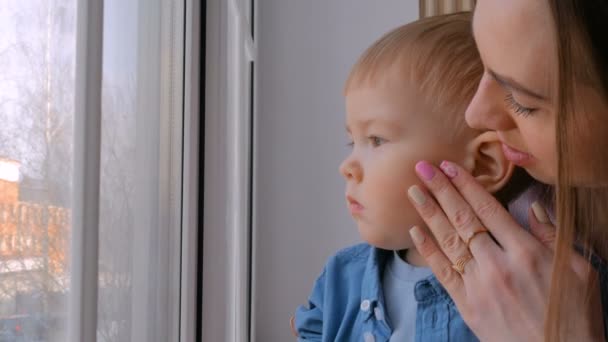 Молодая мать и задумчивый маленький мальчик смотрят в окно — стоковое видео