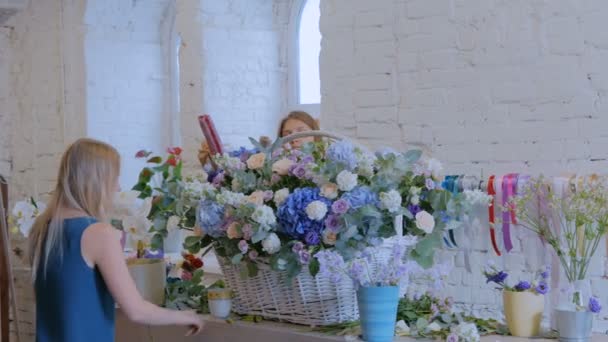 Zwei Floristinnen basteln im Blumenladen einen großen Blumenkorb mit Blumen — Stockvideo