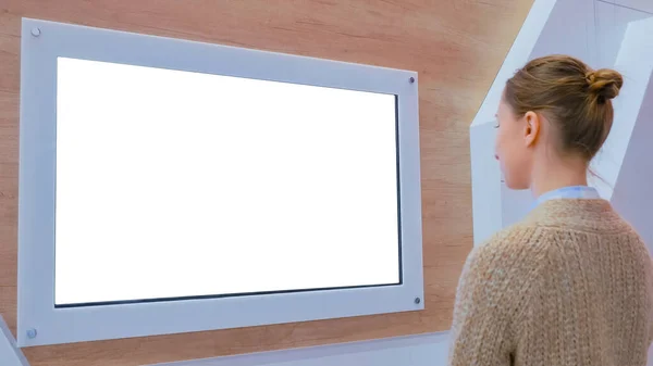 Woman looking at blank white display wall at exhibition - white screen concept