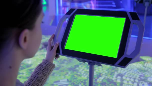 Frau blickt auf am Boden stehenden schwarzen Tablet-Kiosk mit leerem grünen Display — Stockvideo
