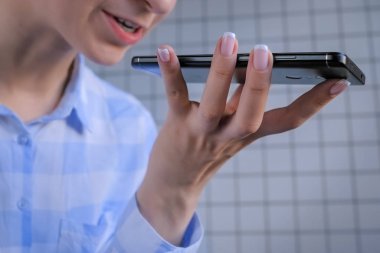Akıllı telefon tutan ve ses tanıma işlevini fayans duvarına karşı kullanan kadın.