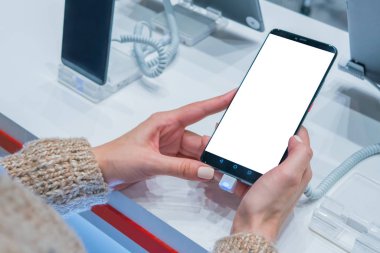 Elektronik mağazasında elinde boş beyaz ekranlı akıllı telefon tutan bir kadın.