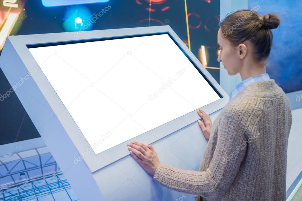 Woman using interactive empty white touchscreen display kiosk at exhibition