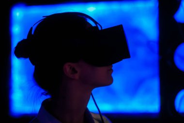 Karanlık etkileşimli sergide sanal gerçeklik kulaklığı kullanan genç bir kadın.