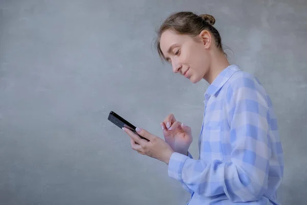 Retrato de mulher em camisa xadrez usando smartphone contra parede cinza — Fotografia de Stock