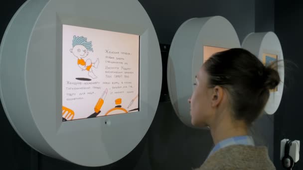 Vrouw kijkt naar wandvertoning en kijkt naar videopresentatie op tentoonstelling — Stockvideo