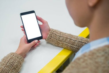 Kafedeki boş beyaz ekranlı akıllı telefona bakan kadın