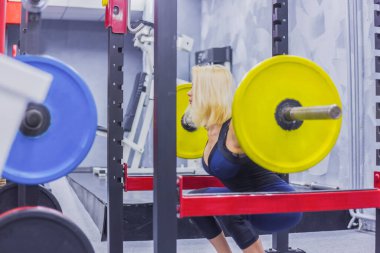 Spor salonunda halterle egzersiz yapan atletik genç bir kadın.