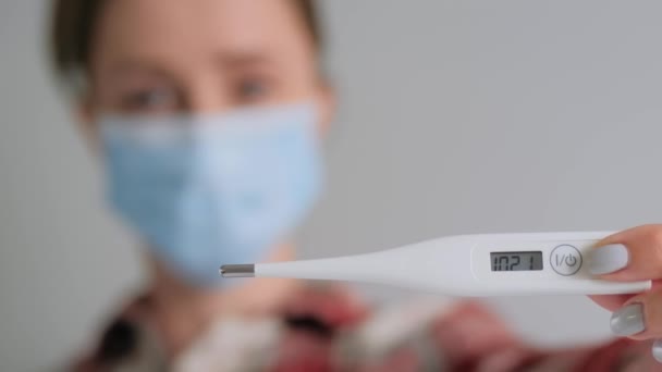 Повільний рух: жінка в медичній масці для обличчя дивиться на медичний термометр вдома — стокове відео