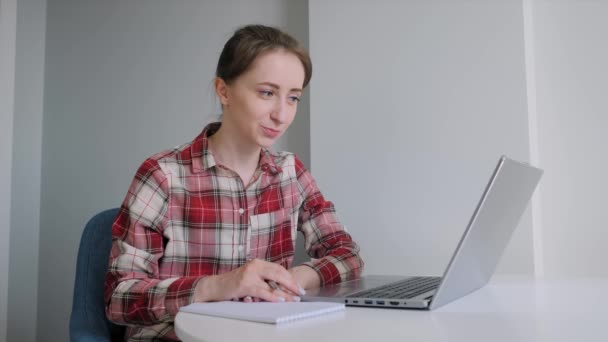 Femme utilisant un ordinateur portable, ayant un appel vidéo en ligne, prenant des notes, parlant à la maison — Video