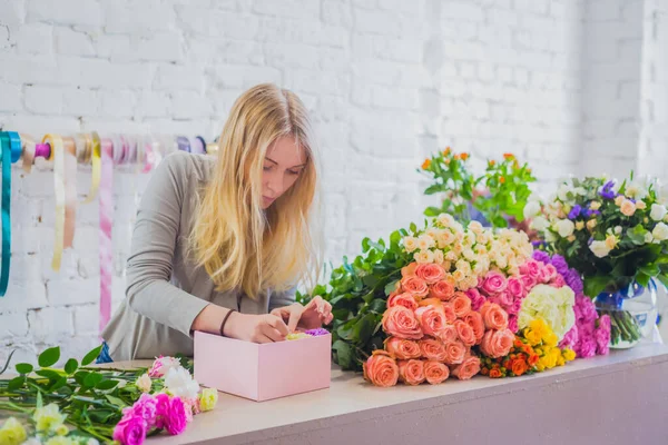 Woman floral artist, florist making gift box with flowers on table