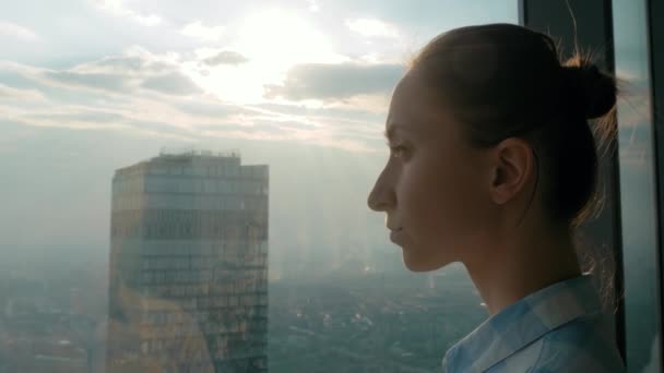 Mujer pensativa mirando paisaje urbano a través de la ventana del rascacielos - vista lateral — Vídeos de Stock