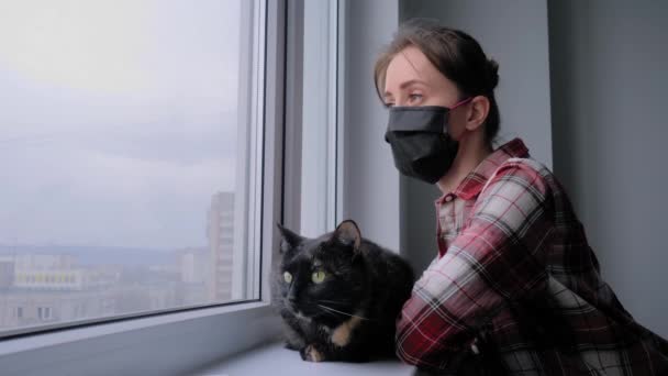 Lassú mozgás: orvosi maszkos nő és fekete macska néz ki az ablakon — Stock videók