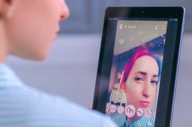 Tablette yüz maskesi olan Snapchat multimedya mesajlaşma uygulamasını kullanan kadın