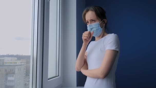 Slow motion: woman with face mask suffering from coughing, looking out of window — Stock Video