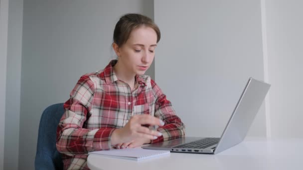 Жінка використовує ноутбук, має онлайн відеодзвінок, робить нотатки, розмовляє вдома — стокове відео