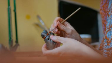 Profesyonel kadın çömlekçi atölyede seramik hatıra düdüğü boyuyor.