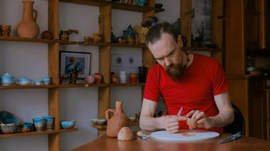 Profesyonel çömlekçi, çömlek atölyesinde özel bir aletle kuru kil bardağı şekillendiriyor.
