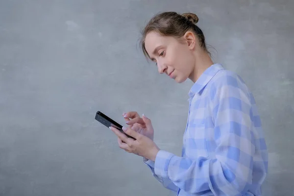 Ritratto di donna in camicia a quadri con smartphone contro parete grigia — Foto Stock