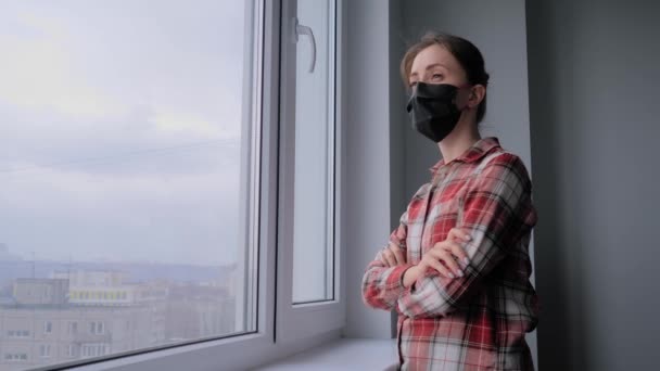 Медленное движение: задумчивая женщина в медицинской маске и выглядывающая в окно — стоковое видео