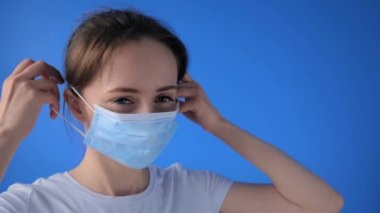 Ağır çekim: kadın tıbbi maske takıyor ve kameraya bakıyor - yakın çekim