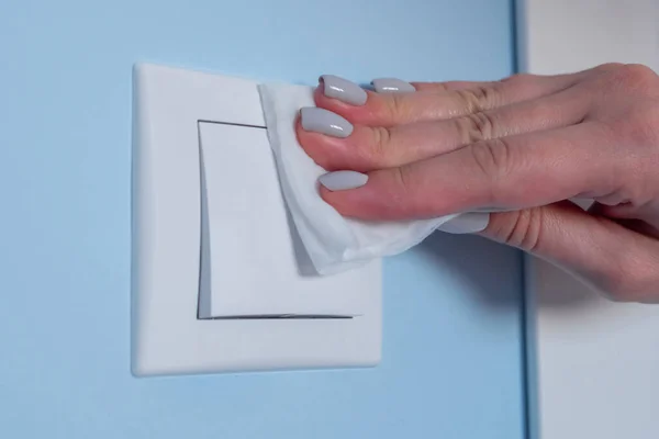 Жінка чистить світло перемикач на синій стіні з мокрою серветкою концепція дезінфекції — стокове фото