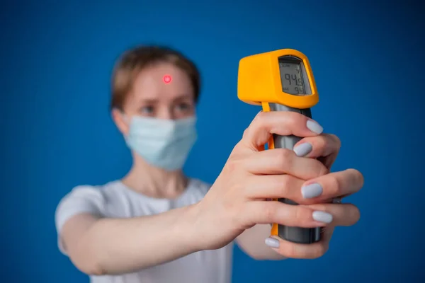 Woman using pyrometer to measure body temperature, blurred background