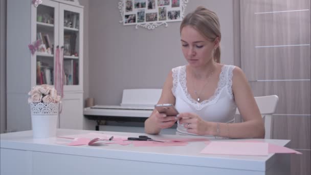 Jonge vrouw met behulp van haar telefoon terwijl het snijden van papier vlinders — Stockvideo