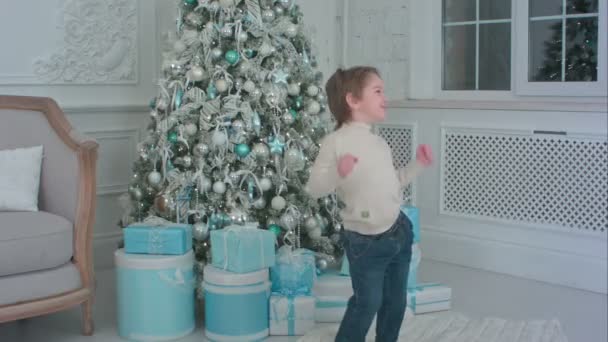 Fröhlicher kleiner Junge tanzt neben Weihnachtsbaum und Geschenken — Stockvideo