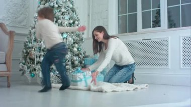 Küçük çocuk annesi hediye kutuları Noel ağacının altına koymak için yardım