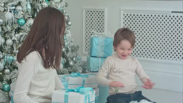 Feliz jovem mãe com bonito pequeno filho brincando com presentes de Natal — Vídeo de Stock