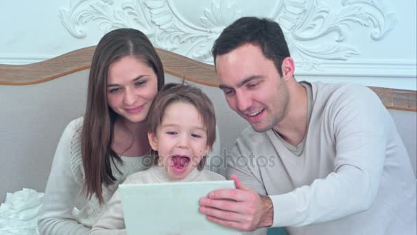 Jeune famille heureuse regardant leurs photos sur la tablette et riant — Video