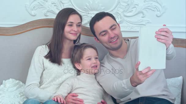 タブレットが付いているソファーで selfies を取って幸せな若い家族 — ストック動画
