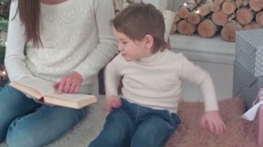Kaprisli çocuğun annesi Noel ağacı yakınındaki bir kitap okuma için dinleme