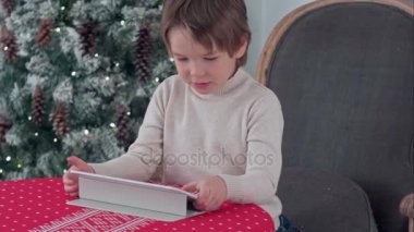 Sevimli küçük çocuk Chirstmas ağaç arka plan üzerinde evde büyük bir koltukta otururken tablet kullanma