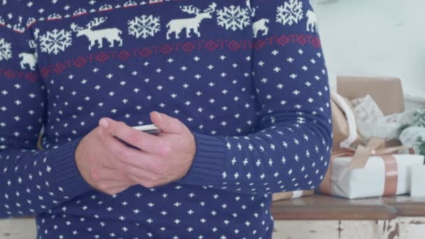 A fiatalember karácsonyi kötöttáru a kezében tartja a telefont — Stock videók