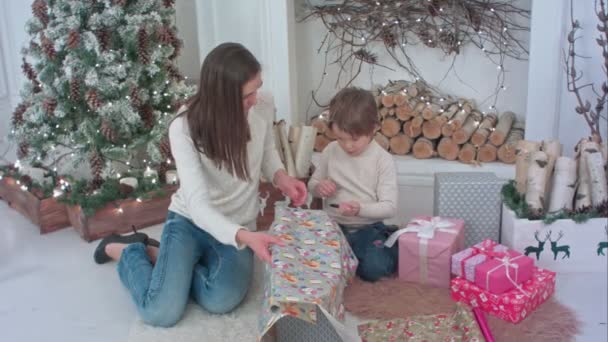 Lindo niño ayudando a su madre a cortar papel para envolver los regalos de Navidad — Vídeo de stock