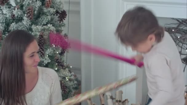 Bonne mère et son fils ayant papier d'emballage épée se battre près du sapin de Noël — Video