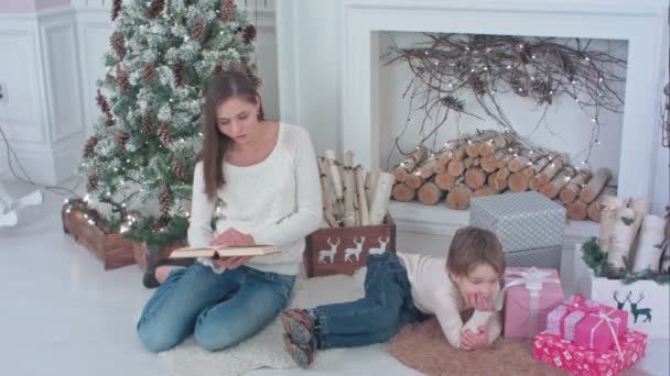 Matka, čtení knihy pro svého malého syna, ležící poblíž vánoční stromeček — Stock video