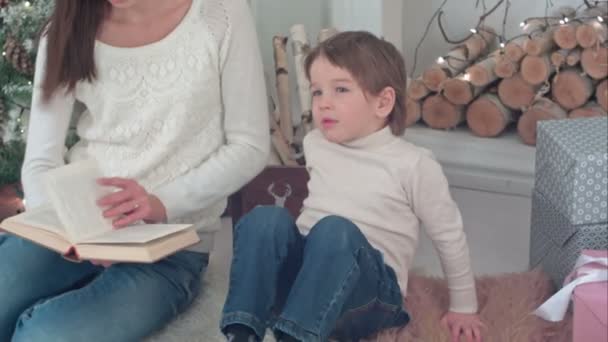 Pequeño niño negándose a leer un libro junto con su madre en la víspera de Navidad — Vídeos de Stock